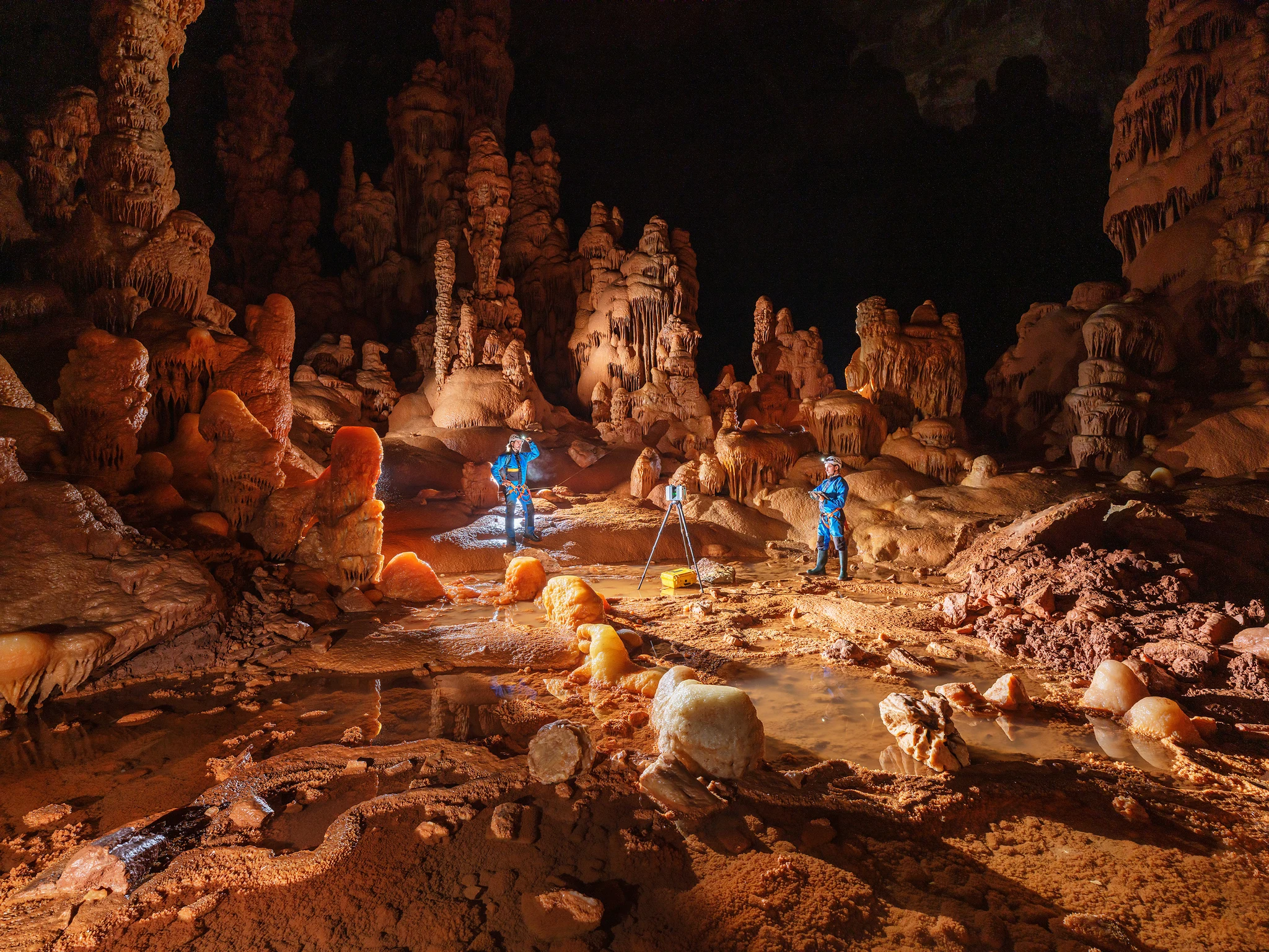 Deux personnes dans une grotte, utilisant des lampes, entourées de formations rocheuses.