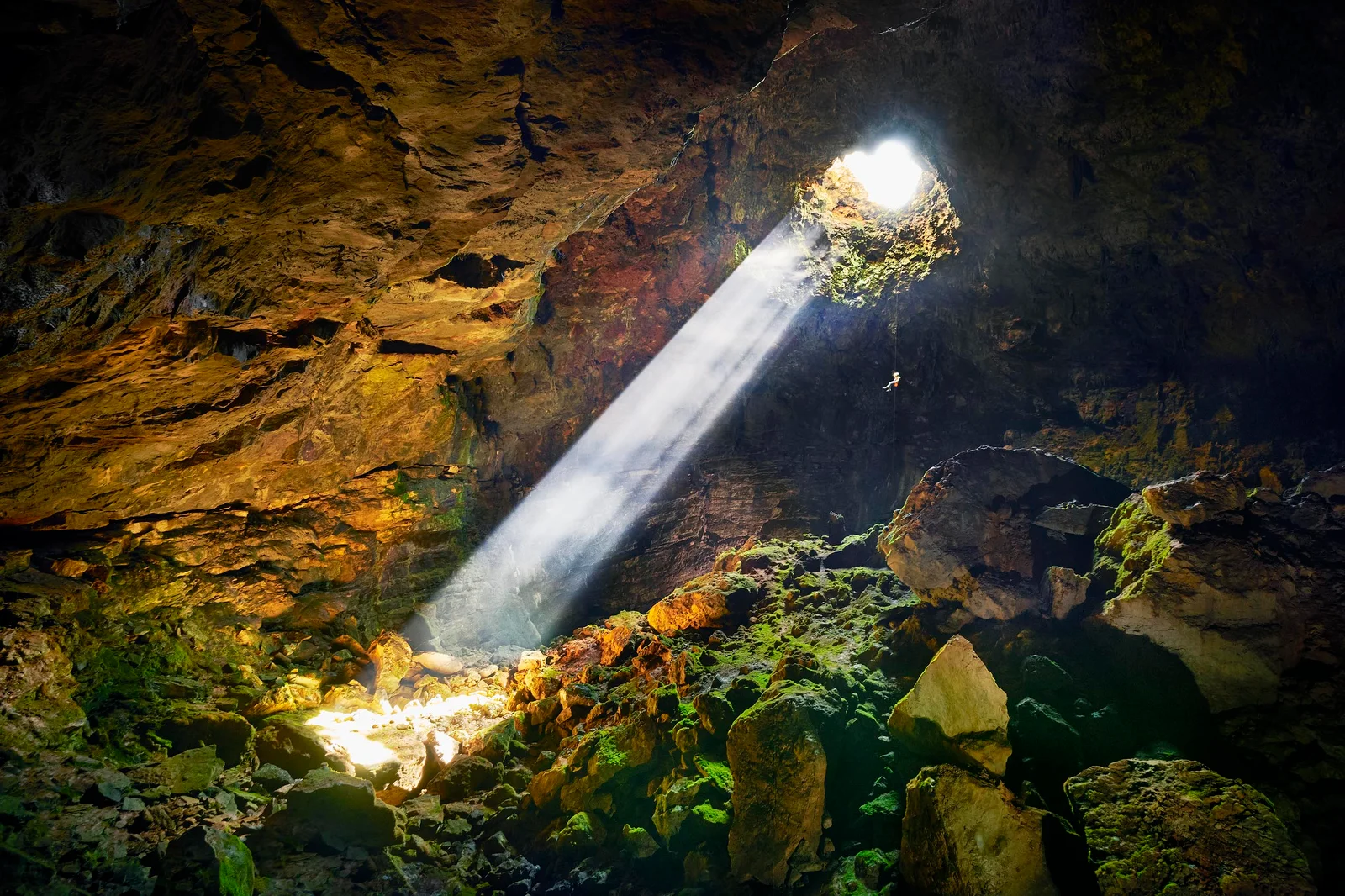 Intérieur d'une grotte avec un faisceau lumineux et des rochers recouverts de mousse.