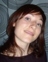 Une femme souriante avec des cheveux bruns devant un fond à motifs circulaires.