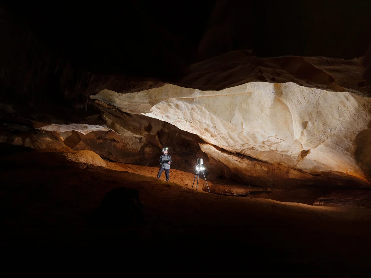 Un spéléologue dans la grotte de Baume Latrone, éclairé par une lampe. Équipement de mesure à proximité.