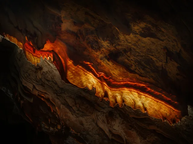 Formation rocheuse avec stries orange et jaunes sur fond sombre, montrant des textures marquées et des reflets de lumière.