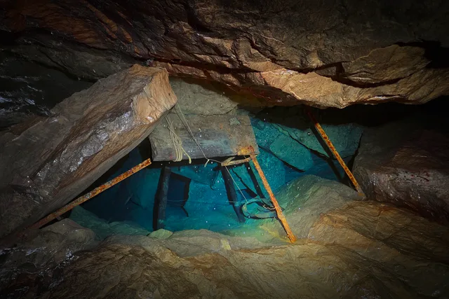 Galerie souterraine inondée avec vestiges d’aménagements et structures métalliques immergées.