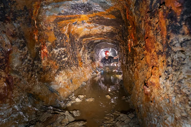 Opérateur dans une ancienne galerie minière de l’Hérault, étroite, minéralisée et partiellement noyée.