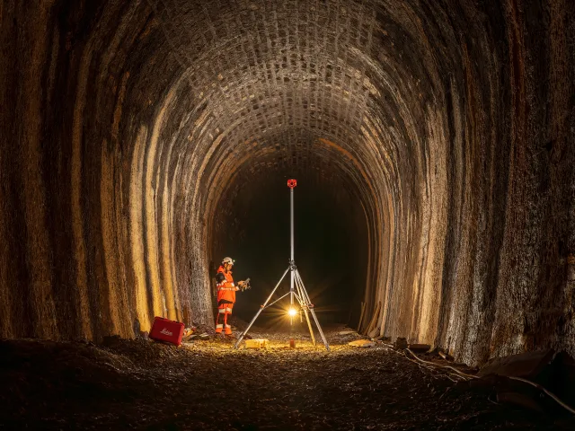 Un travailleur dans un tunnel utilise un instrument sur trépied avec une lampe à proximité.