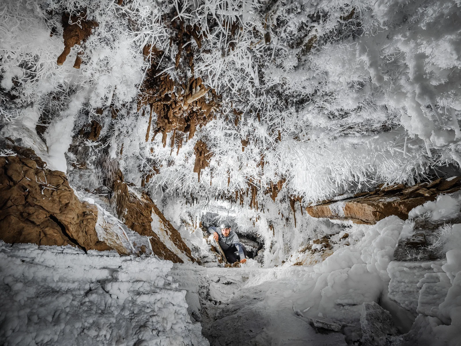 Un spéléologue escalade dans une grotte ornée de formations de glace et de stalactites.