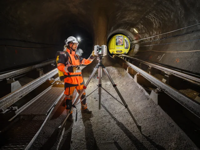 Technicien dans un tunnel avec un scanner 3D et un train jaune en approche.