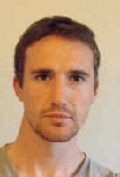 Homme avec cheveux bruns, portant un t-shirt gris, fond beige.